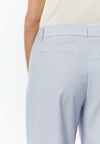 Hellblaue, maßgeschneiderte Hosen mit glatter Textur, Gesäßtaschen und einem schlanken Bund, die dezente Stickdetails aufweisen.