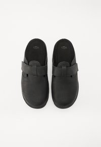 Zapatos negros de tipo slip-on, hechos de suave ante, con una correa en la parte superior. Punta redondeada y plantilla acolchada para mayor comodidad. Acabado liso y mate.