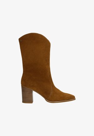 Hnědá semišová kotníková bota s špičatou špičkou a mírně zakřiveným vrškem. Disponuje vrstveným dřevěným podpatkem a viditelnými švy.