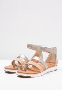 Para damskich płaskich sandałów z metalicznej skóry i korkowych pasków, z zapięciem na kostkę, miękką podeszwą i białą wyprofilowaną podeszwą.