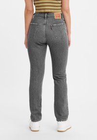 Jeans de tiro alto gris con una textura desgastada, diseño de cinco bolsillos y detalles de costura. Llevados con una blusa a rayas y zapatos blancos.