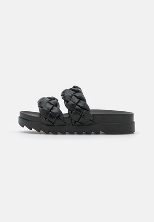 Black sandals with woven straps, featuring a chunky platform sole and a zigzag tread pattern. Material appears smooth and leather-like.