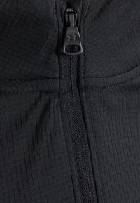 Černý zippered oděv má ribbovanou texturu a hladký doplněk na zip. Tkanina se zdá být lehká a flexibilní.