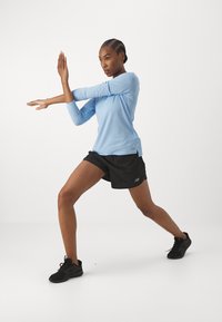 Light blue long-sleeve shirt paired with black shorts. The shirt features a relaxed fit and subtle logo; shorts have an elastic waistband.