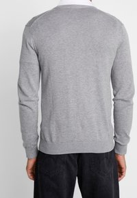 Maglione grigio lavorato a maglia con maniche lunghe, orlo e polsini a coste, e una texture liscia. Presenta un collo rotondo e un design minimalista.