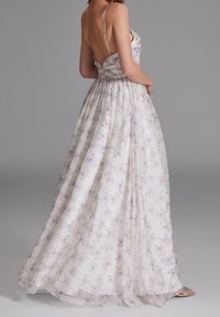 Lungo vestito floreale realizzato in tessuto leggero, bianco con accenti viola. Presenta spalline sottili, un corpetto aderente e una gonna fluida.
