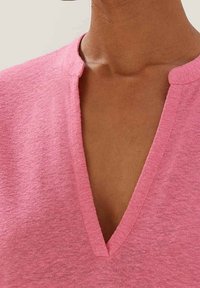 Rosa V-ringad topp i mjukt, texturerat tyg; har en grund krage och en avslappnad passform.