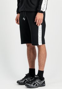 Shorts de sport noirs avec un imprimé blanc "INDUSTRIES" sur le côté, fabriqués en tissu doux. Portés avec des baskets noires et des chaussettes.
