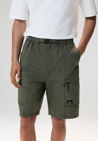 Pantaloncini cargo con vita elasticizzata in verde oliva, caratterizzati da una finitura testurizzata, multiple tasche e una cintura con fibbia nera.