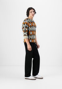 Mønstret ullgenser med oransje, grå og svarte geometriske design; avslappet passform; kombinert med svarte bukser og hvite joggesko.