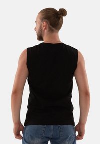 Schwarzes, ärmelloses Hemd mit Rundhalsausschnitt, aus weichem Stoff, kombiniert mit blauen Jeans. Einfaches Design, ohne sichtbare Muster oder Grafiken.