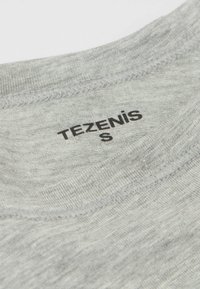 Šedá tkanina trička s hladkým povrchem; má kulatý výstřih a černě potištěnou cedulku 'TEZENIS S' blízko límce.