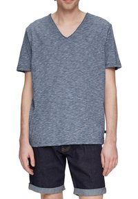 T-shirt z krótkim rękawem, w serek, wykonany z niebieskiego, melanzowego materiału. Koszulka ma luźny krój i jest zestawiona z ciemnymi szortami dżinsowymi.