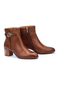 Botas de cuero marrón hasta el tobillo con punta redonda, detalles en dorado y cremallera lateral. Con un tacón de madera texturizada.