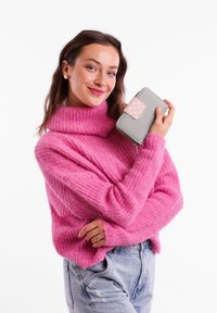 Gray wallet with pink polka dot flap and zip closure, held against a pink textured sweater. The wallet is compact and rectangular.