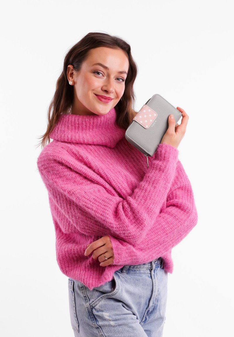 Gray wallet with pink polka dot flap and zip closure, held against a pink textured sweater. The wallet is compact and rectangular.