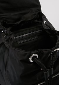Sac à cordon noir en tissu durable. Doté d'œillets en métal argenté, de poignées en corde tressée et d'une poche zippée intérieure pour une meilleure organisation.
