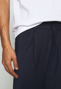 Marineblauwe broek met een rechte voorkant, elastische tailleband en zijzakken. De stof lijkt glad en heeft een lichte textuur.
