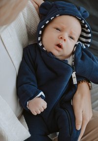 Marineblaues Babystrampler mit Kapuze in Bärenohrform, Reißverschluss und gestreifter Fütterung. Verfügt über eine gerippte Textur und kontrastierende weiße Bündchen.