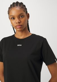 Black cotton t-shirt featuring a round neck, short sleeves, and a white "BOSS" logo printed centrally on the front.