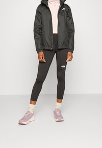 Svart lättviktsjacka med huva, ljusrosa zip-up topp, svarta leggings och rosa löparskor med ljusa accenter. Vit logotyp på leggings.