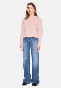 Maglione lavorato a maglia rosa chiaro con scollo rotondo, abbinato a jeans blu a vita alta svasati con tasche frontali e una finitura scolorita.