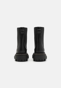 Botas negras hasta el tobillo con un acabado de cuero suave, parte superior de tela texturizada, suelas de goma gruesa y un acento metálico decorativo en el tacón.