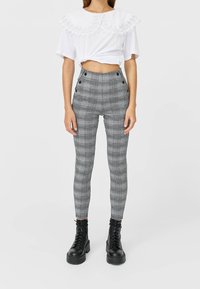 Pantaloni a vita alta a quadri bianco e nero con dettagli a bottoni, abbinati a un top corto bianco con colletto rifinito in pizzo.