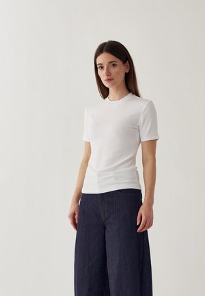 Baltas trumpomis rankovėmis marškinėlis su apvalia iškirpte, aptemptas dizainas ir švelni, minkšta tekstūra, derinamas su tamsiais plačiomis kojomis džinsais.