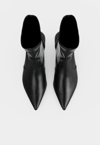 Paire de bottines noires à bout pointu avec une finition en cuir lisse, vue de dessus sur fond blanc.