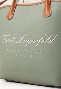 Grønn teksturert totebag med brune skinnhåndtak. Har hvit brodert logo og tekst: "Karl Lagerfeld 21 RUE ST-GUILLAUME PARIS."