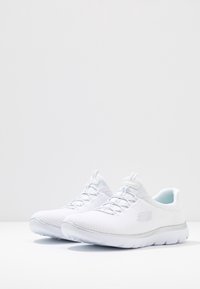 Scarpe da ginnastica bianche con upper in rete, caratterizzate da un design testurizzato, lacci e una suola imbottita con un sottile dettaglio argentato.
