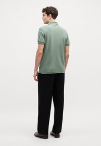 Grønn polo skjorte med avslappet passform, korte ermer og enkel krage, kombinert med svarte bukser og brune sko. Strukturert stoff.