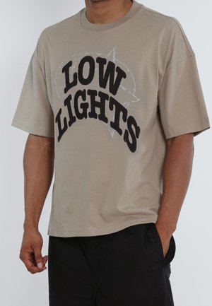 Beige T-Shirt mit kurzen Ärmeln und einem großen schwarzen "LOW LIGHTS"-Grafik. Hergestellt aus weicher Baumwolle, mit lässiger Passform und rundem Halsausschnitt.