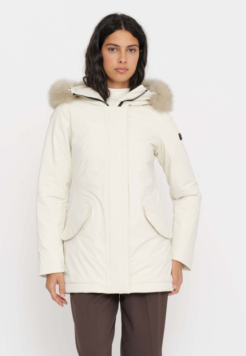 Parka bianca isolata con cappuccio foderato in pelliccia, chiusura con zip e tasche laterali. Tessuto liscio con dettagli di cucitura sottili su tutta la superficie.