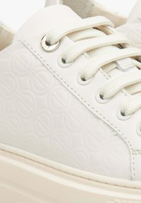 Białe trampki z wytłoczonym wzorem logo, okrągłymi sznurowadłami i metalowymi oczkami. Gładki materiał z teksturowanym wykończeniem i masywną podeszwą.