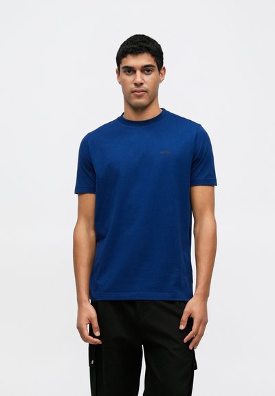 T-shirt en coton bleu avec un col rond, des manches courtes et un petit logo sur la poitrine. Associé à un pantalon cargo noir.