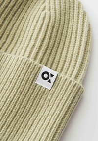 Light beige ribbed knit beanie with a folded edge and a white rectangular label featuring a black geometric logo.