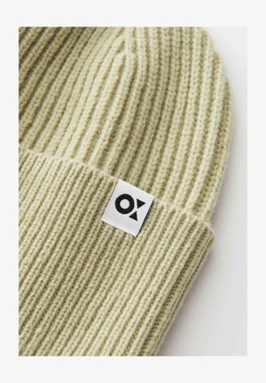 Hellbeige ribbed Strickmütze mit umgeschlagenem Rand und einem weißen rechteckigen Etikett mit einem schwarzen geometrischen Logo.