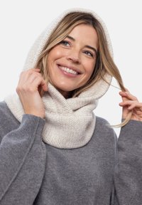 Dzianinowy szal z kapturem w kolorze kremowym, z prążkowaną teksturą. Nosi się go na szarym swetrze, podkreślającym miękką tkaninę i dopasowany krój.