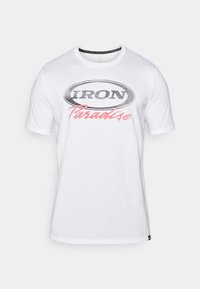 Bílá bavlněná tričko s černým oválným logem, na kterém je „IRON“ a růžovým nápisem „Paradise“. Krátké rukávy a kulatý výstřih.