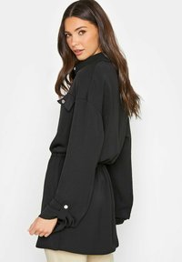 Zwarte jurk met lange mouwen, getailleerde taille en knoopmanchetten. Heeft een ontspannen pasvorm en zachte textuur. Geen zichtbare patronen of accenten.