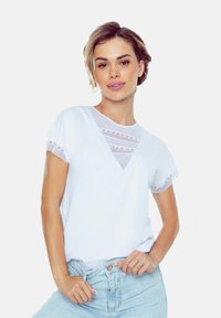 Biała bawełniana koszulka z krótkimi rękawami ozdobionymi koronką i dekoltem w serek. Materiał jest gładki i ma luźny krój.