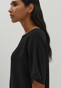 Top nero con scollatura rotonda e maniche a tre quarti, caratterizzato da un tessuto testurizzato e una vestibilità ampia, visto di lato.