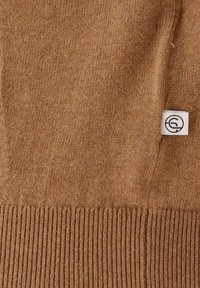 Brown knit sweater with a ribbed hem. Features a small, white label with a logo. Soft texture, medium weight, and no visible patterns.