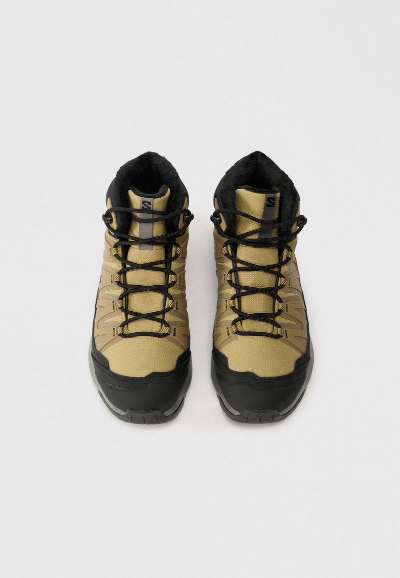 Khaki wandelschoenen met een gestructureerde stofbovenkant, zwarte rubberen zolen en zwarte veters, voorzien van een gevoerde kraag en een versterkte neus.