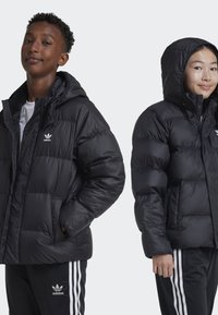 Black puffer jacket with a hood, featuring a quilted design, lightweight material, and an embroidered logo on the chest; paired with black pants.