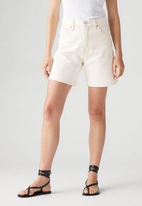 Σορτς από τζιν σε εκρού χρώμα με ψηλή μέση, πέντε τσέπες και αντίθετες ραφές, συνδυασμένα με μαύρα σανδάλια με λουράκια.