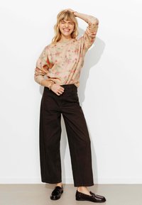 Pull en tricot rose clair à motif floral, coupe décontractée ; associé à un pantalon noir taille haute à jambes larges et des mocassins noirs.