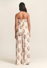 Be rankovių, kremine palaidine su surinkta nugara, derinama su plačiomis kelnėmis su rudais gėlių raštais. Lengva medžiaga ir laisvas siluetas.